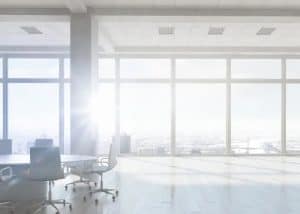 Modern office with panoramic city views, sunlight streaming through large glass windows, and spacious environment.